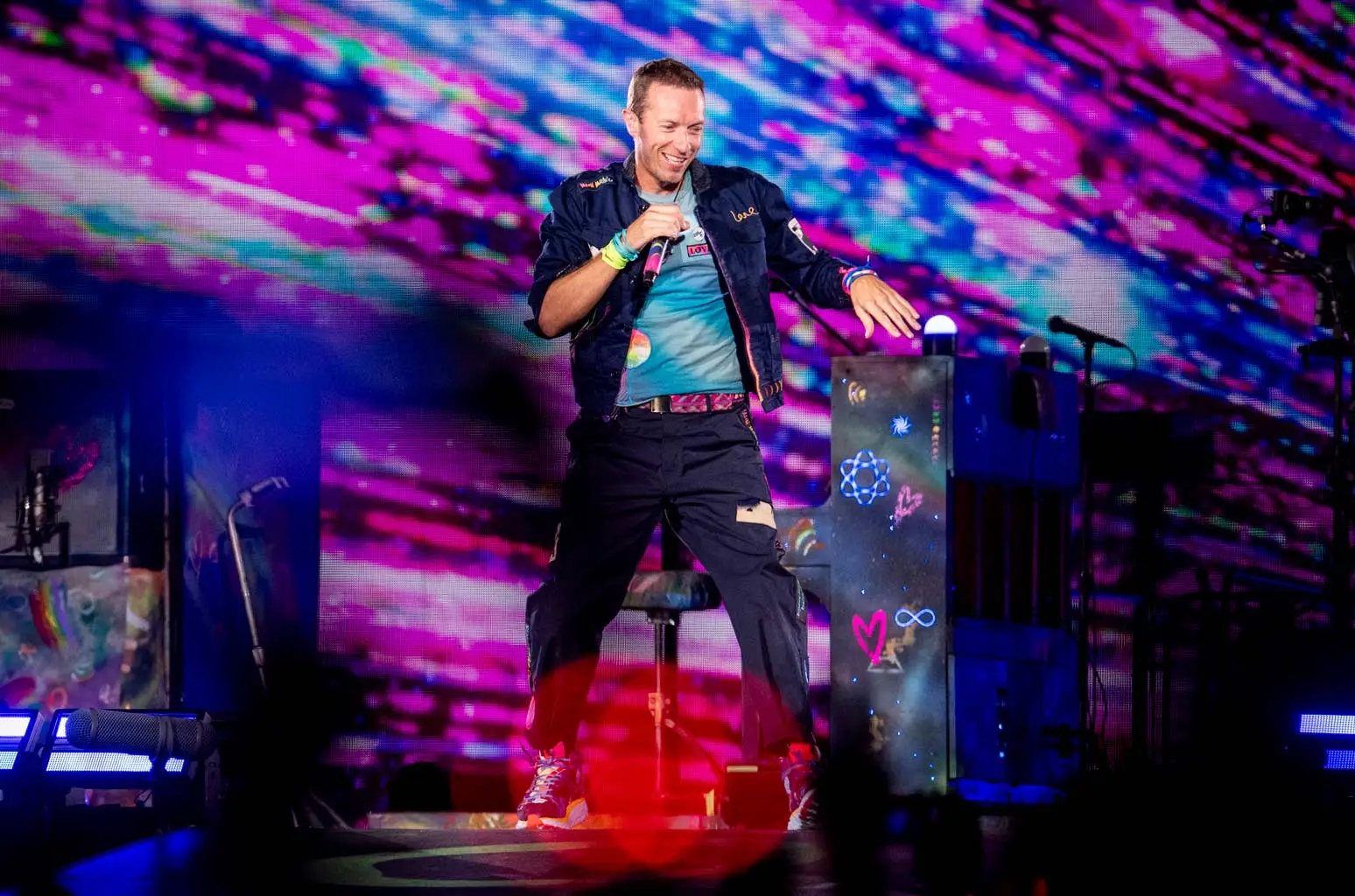 Chris Martin performing in Rome during the Music of the Spheres tour, pink and teal stage visuals behind him